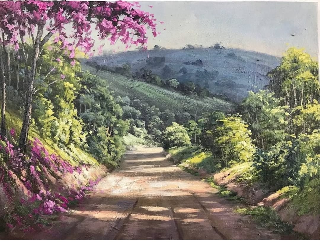 Caminho de terra com ipês rosa e montanhas